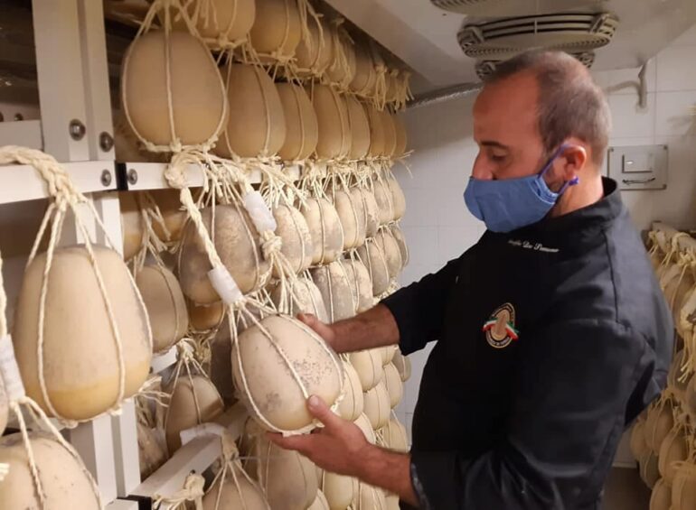 Foto di un artigiano che controlla la stagionatura di una forma di Provolone del Monaco DOP.